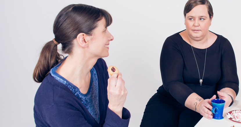 Två glada kvinnor vid ett fikabord. Foto.