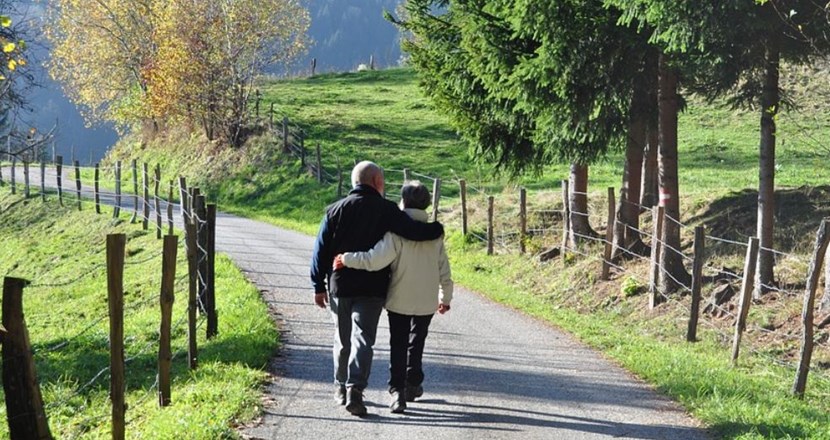Ett äldre par som är ute och promenerar på en grusväg i vacker natur. De håller om varandra.