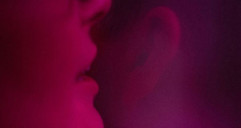 Sensuell närbild i rött ljussken där någon viskar i ett öra.