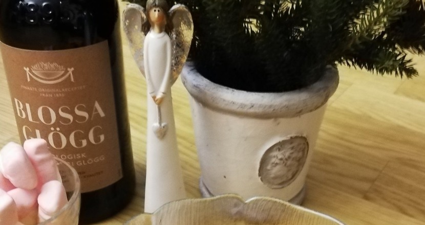 En bild med lussekatter, en flaska glögg, ett glas med skumtomtar, en ängel och en kruka med en gran. Foto.