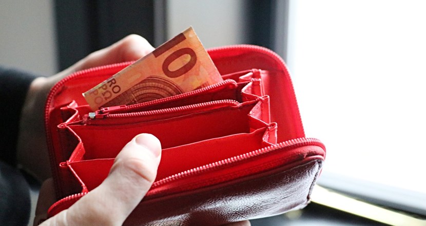 Två händer som håller i en röd plånbok med bara en sedel i. Foto.