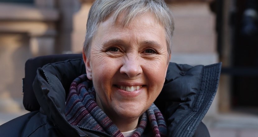En ansiktsbild av Lise Lidbäck, Neuros ordförande, en leende medelålders kvinna med kort blont hår i en mörk täckjacka och en mönstrad halsduk. Foto.