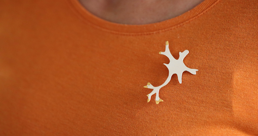 En silverbrosch på en orange tröja. Foto.