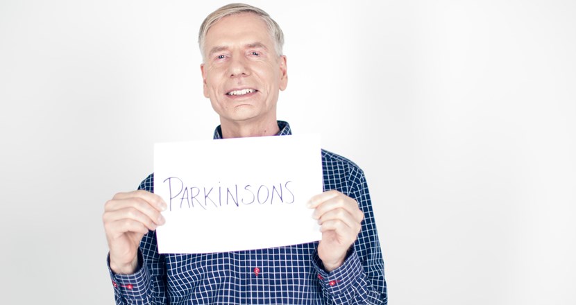 En man ser glad ut och visar skylt med Parkinsons sjukdom