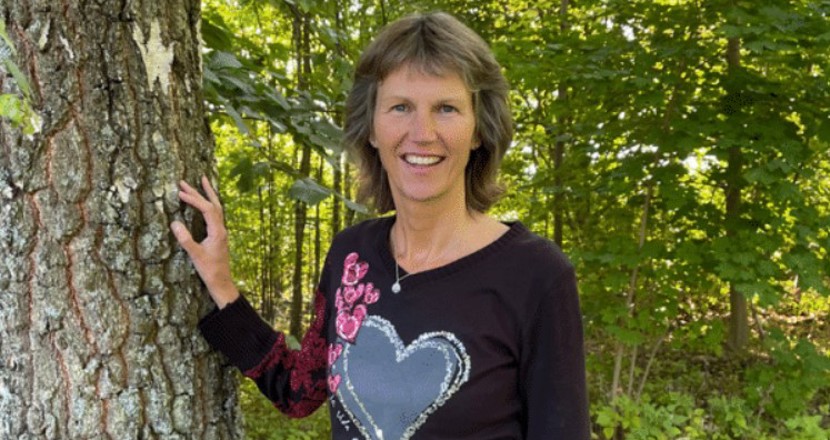 Carina fotograferad utomhus i det gröna med ena handen på en trädstam. Foto.