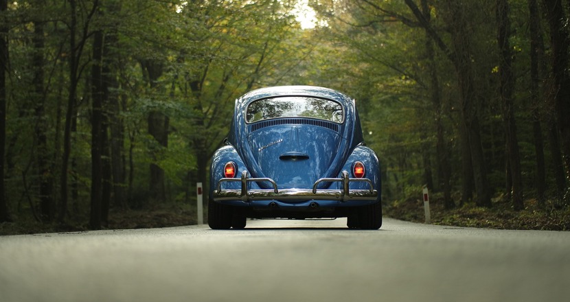 En blå Volkswagen bubbla sedd bakifrån på en väg kantad av grönskande träd. Foto.