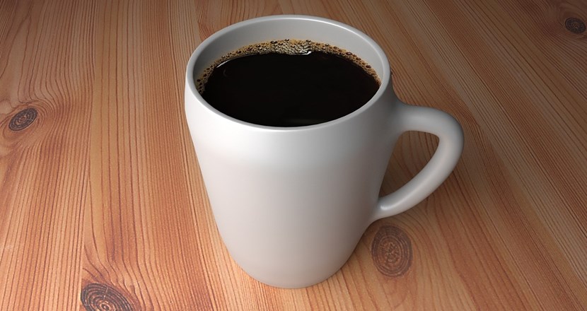 en vit kaffekopp med svart kaffe på bordskiva av trä