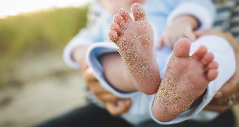 Två spädbarnsfötter med sand under fotsulorna. Foto.