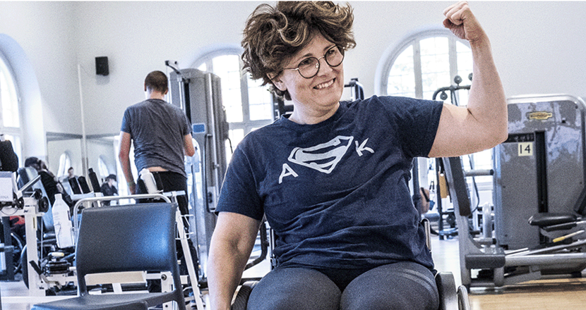 Bild som visar överkroppen på en glad kvinna som sitter och tränar styrka. Foto.