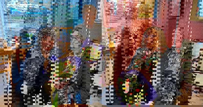 Tre sittande kvinnor med varsin fin blombukett.