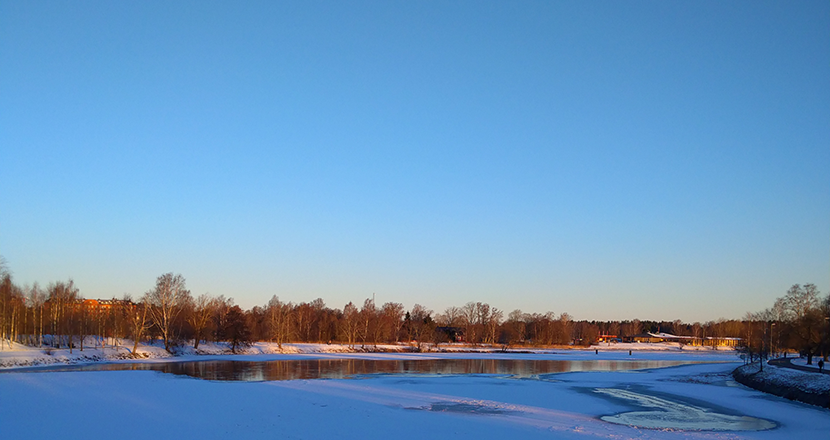 En vinterbild över Klarälven och i fronten ett staket, men bilden visar mest blå himmel  och blåtonad is.
