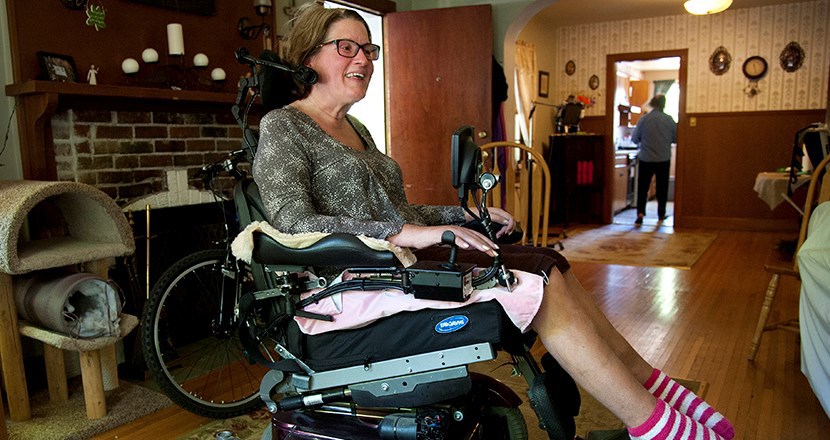 En kvinna som sitter i en permobil som har korta rosa-och-vitrandiga sockor. Foto.