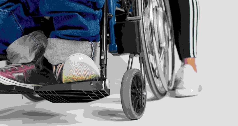 Närbild på fötter i rullstol och gående. Foto.