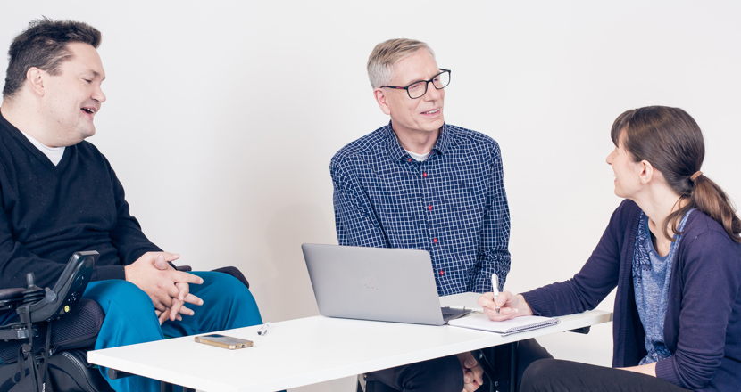 Grupp med två män och en kvinna vid pc som diskuterar.