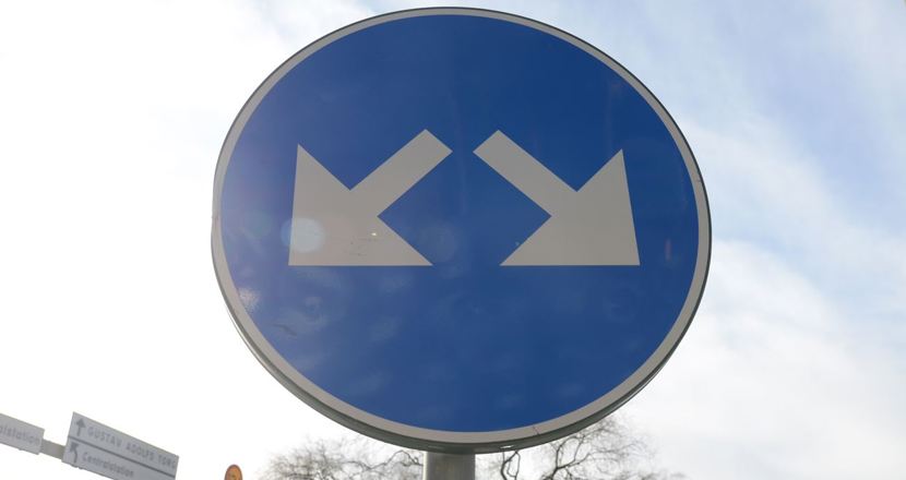 Blå vägskylt med två vita pilar.