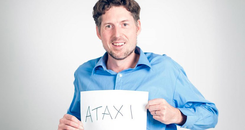 Man i blå skjorta håller upp en skylt med texten ataxi.