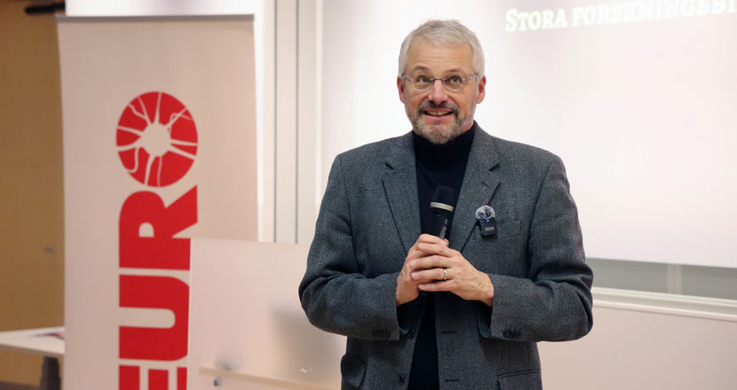 Peter Andersen står klädd i kavaj och pratar i en mikrofon. Foto.