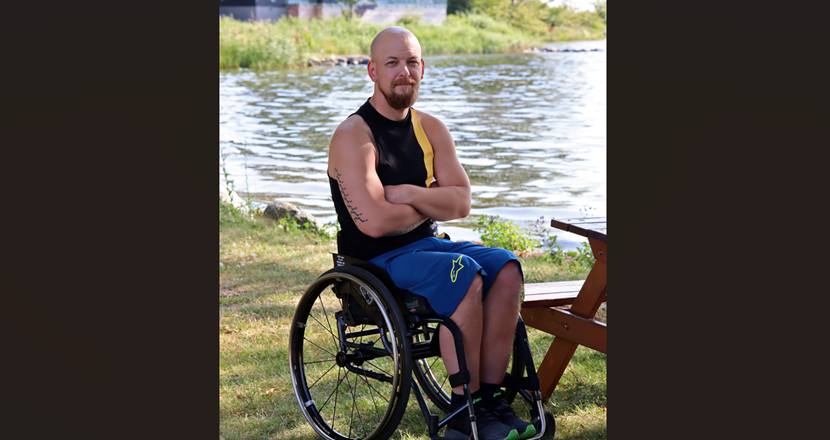 Tomas sitter i en rullstol i strandkanten en sommardag i solsken.