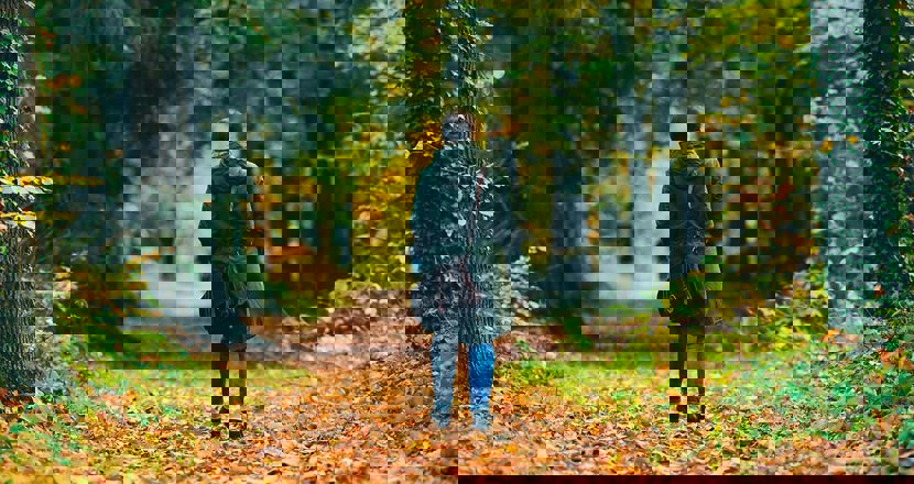 En kvinna går på en skogsstig full med höstlöv, med ryggen mot oss. Foto.