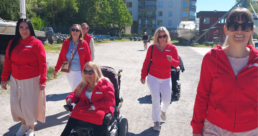 Kanslipersonalen på promenad i solen, klädda i röda neuro tröjor. Foto.