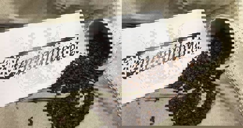 En skylt med Wienerkonditoriet och en vält mugg med kaffebönor på ett beige tyg. Foto.