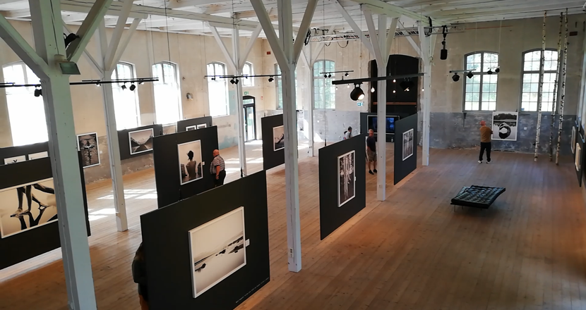 En överblicksbild på konsthallen Sliperiet med fotoutställningen och stora takbjälkar. Foto.