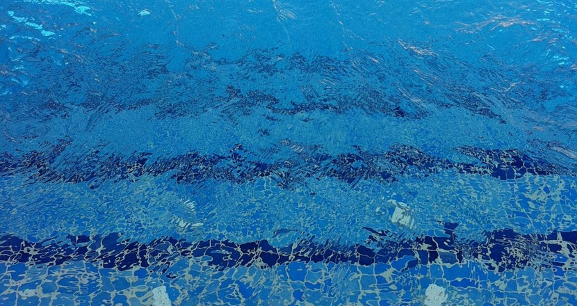 Vatten i en bassäng där det blå kaklet i botten syns. Foto.