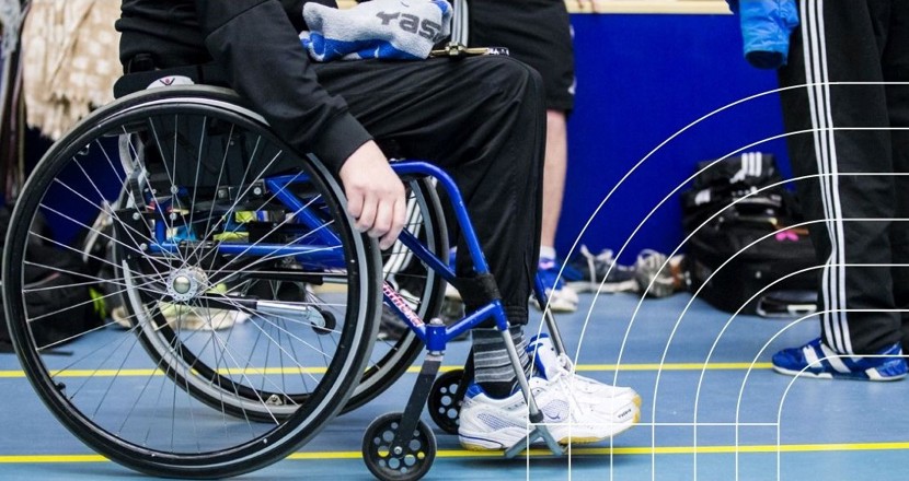 Nederdelen av en person i träningskläder, som sitter i en blå rullstol. Foto.