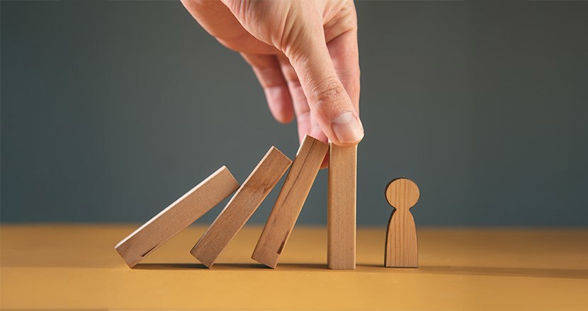 Händer som håller emot när träpinnar håller på att falla över en liten trägubbe. Foto.