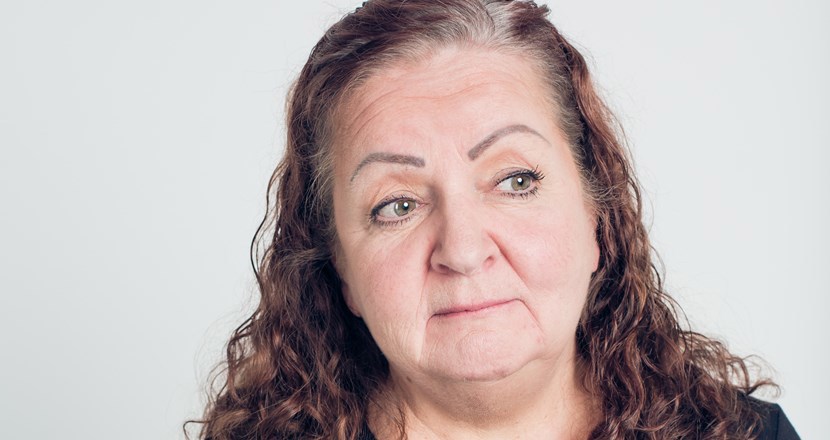 Huvudet på en medelålders kvinna med långt hår tittar mot dig. Foto.