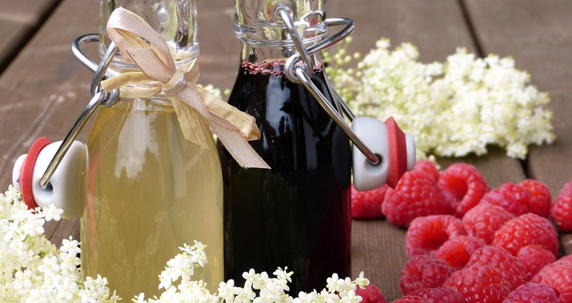 Saft och gammeldansk och några hallon och fläder står på ett bord. Foto.