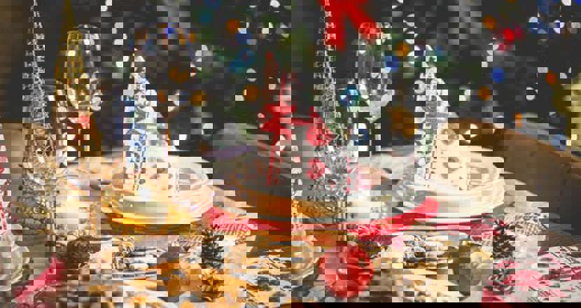 Bild på ett dukat julkuvert, med två glas och en jultalrik med en julservett på. Ett stort fat med pepparkakor är framdukat. I bakrunden står en grön välpyntad gran.