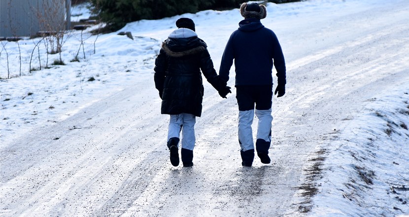 Två personer bakifrån som går på en isig väg och håller varandra i händerna. Foto.