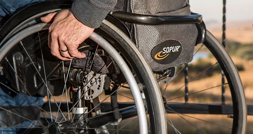 Närbild på ett rullstolshjul sett bakifrån, en hand på hjulet. Foto.