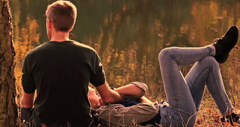 Sittande man vilar sin hand på kvinna som ligger i hans knä utomhus i naturen