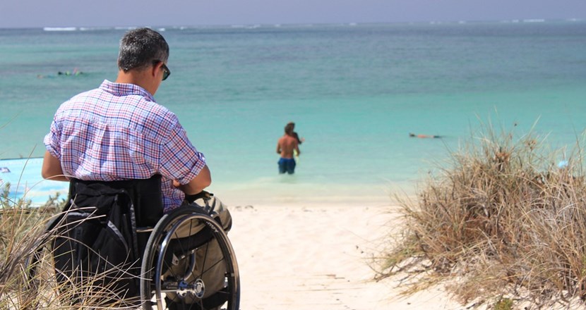 En man i en rullstol vid en sandstrand. Foto.