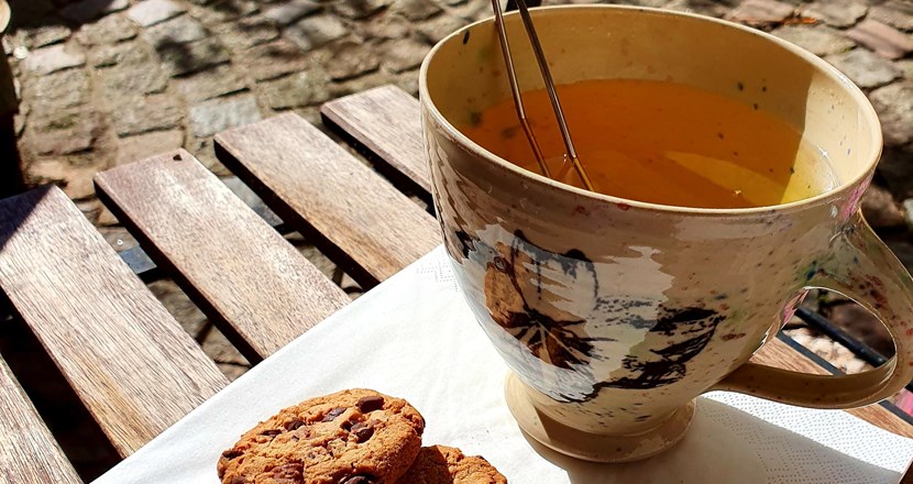 En kopp te med 2 chokladkakor på en servett serverad ute i solsken.