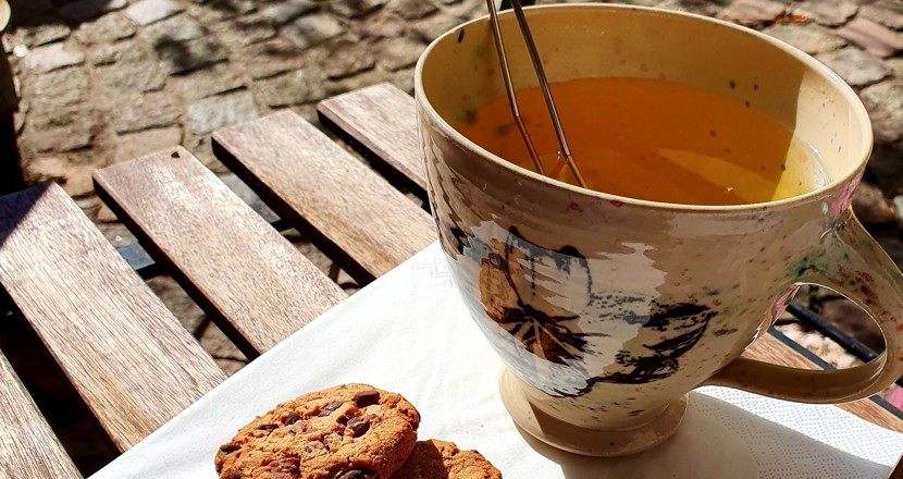 En kopp te med 2 chokladkakor på en servett serverad ute i solsken.