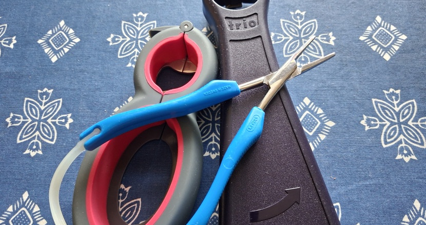 Tre stycken småhjälpmedel som ligger på en blå duk med ett vitt mönster. Foto.