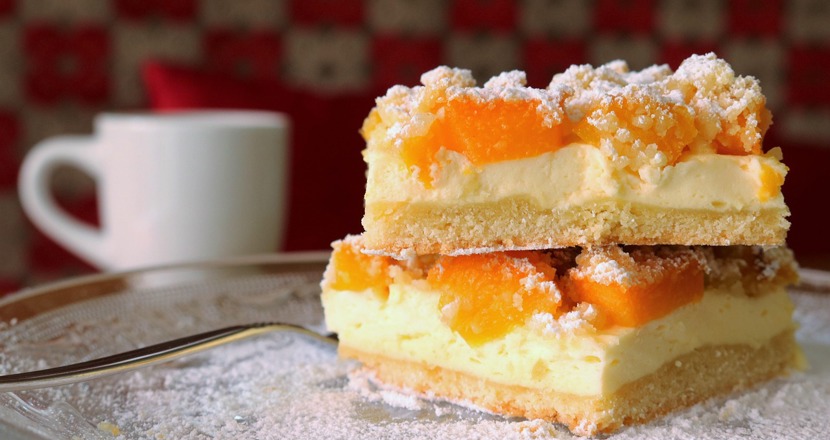 Två tårtbitar med aprikoser och en vit kaffemugg. Foto.