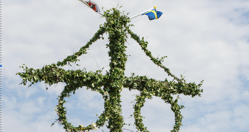 Övre delen av en lövad midsommarstång med ett kors med två kransar. Foto.