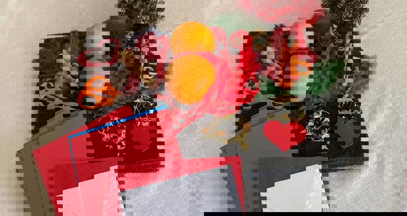 Ett foto med pysselmaterial. Tovplatta, ull, nålar, saxar. Två apelsiner, röda sidenband, rött trähjärta, röda kort och kuvert