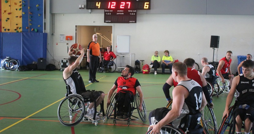 Personer i rullstol som spelar basket i en sporthall. Foto.